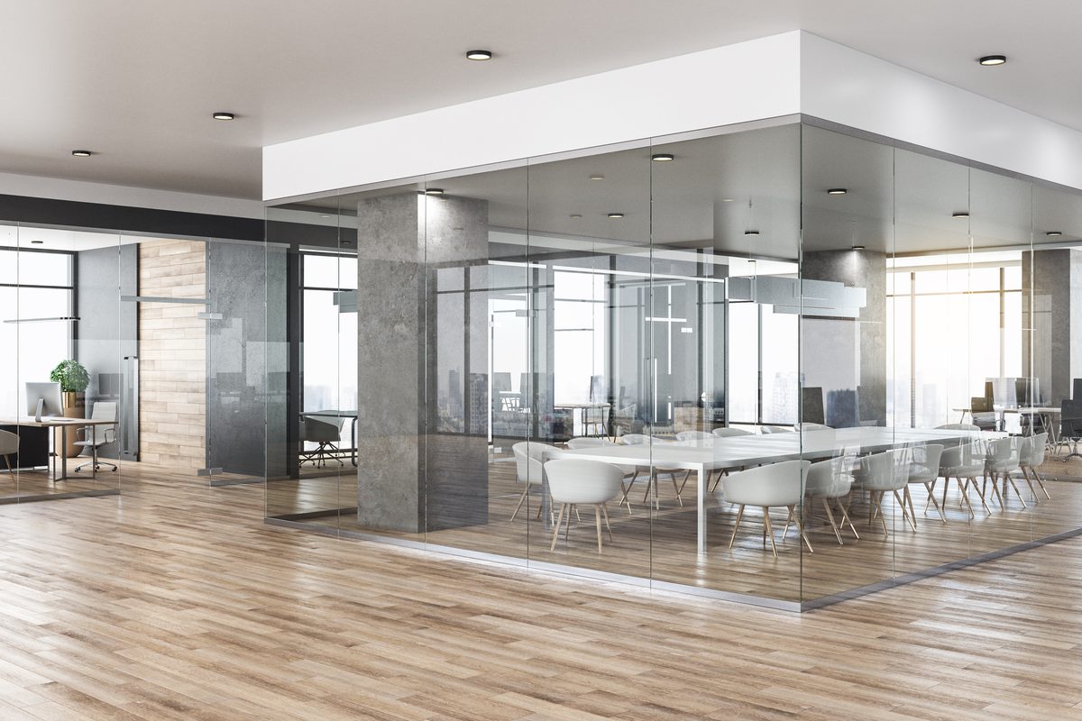 Glass-walled meeting rooms with white chairs around long tables, in an office with timber-look floors and recessed ceiling lights